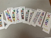 A top-down view of several paper bookmarks spread across a gray table. The bookmarks are decorated with drawings of bookshelves, plants, and stars, with the words "World Read Aloud Day" colored in various bright markers by students.