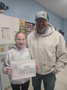 A man in a tan "Carhartt" hoodie and a grey baseball cap stands with a girl in a pastel tie-dye hoodie and glasses. They are holding a sign that reads "WE CRACKED THE CODE" with a key ring illustration.